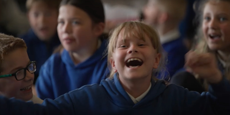 Group of children singing in blue hoodies with blurred faces, gathered closely together.
