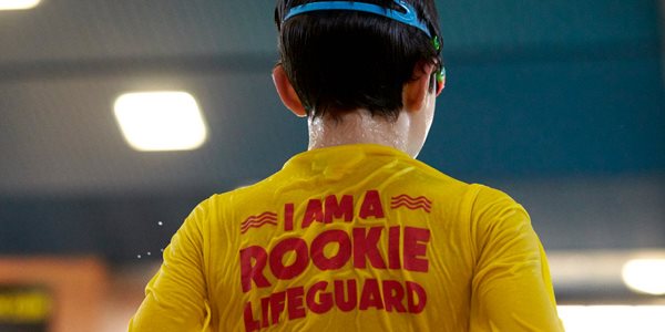A young person wearing a yellow t-shirt with red writing. I am a rookie lifeguard