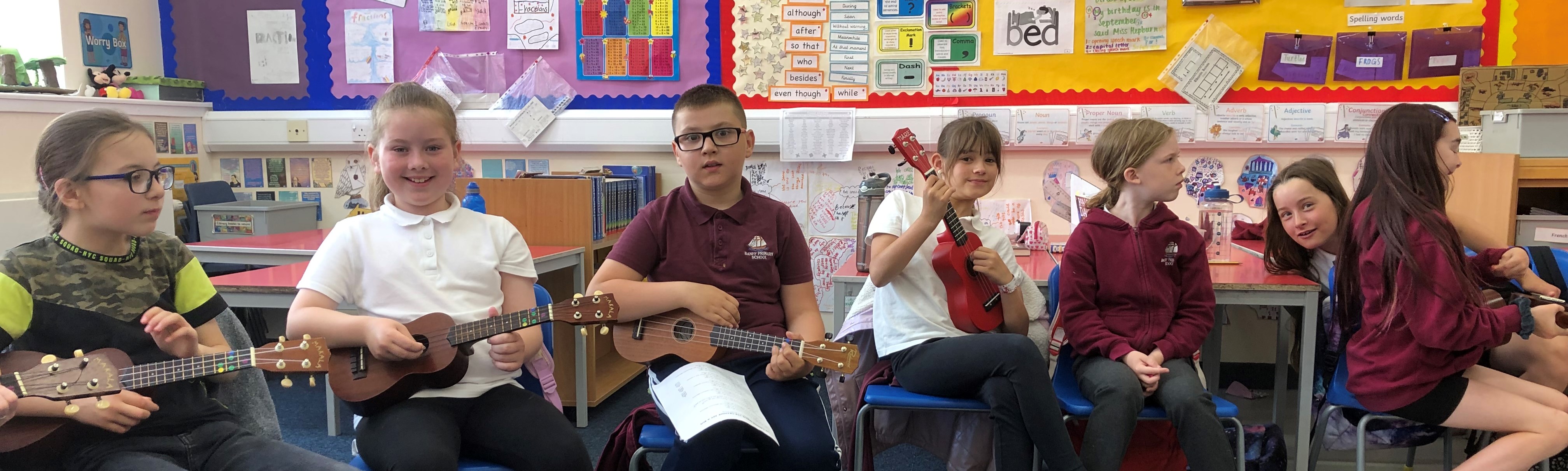 7 primary school children sitting in a row playing Ukulele